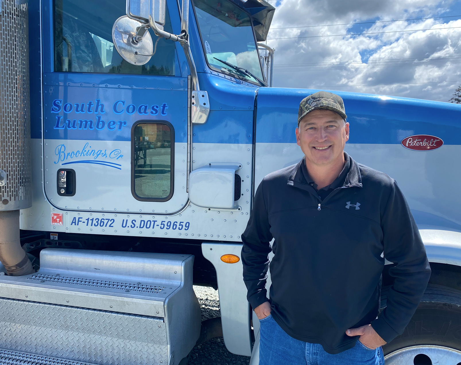 A South Coast Lumber Employee stands in front of a logging truck